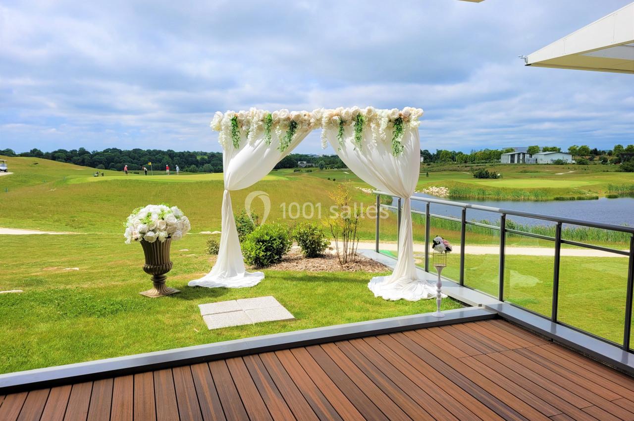 Arche de mariage décorée de fleurs blanches et tissu, installée sur une pelouse près d'un lac par temps clair.