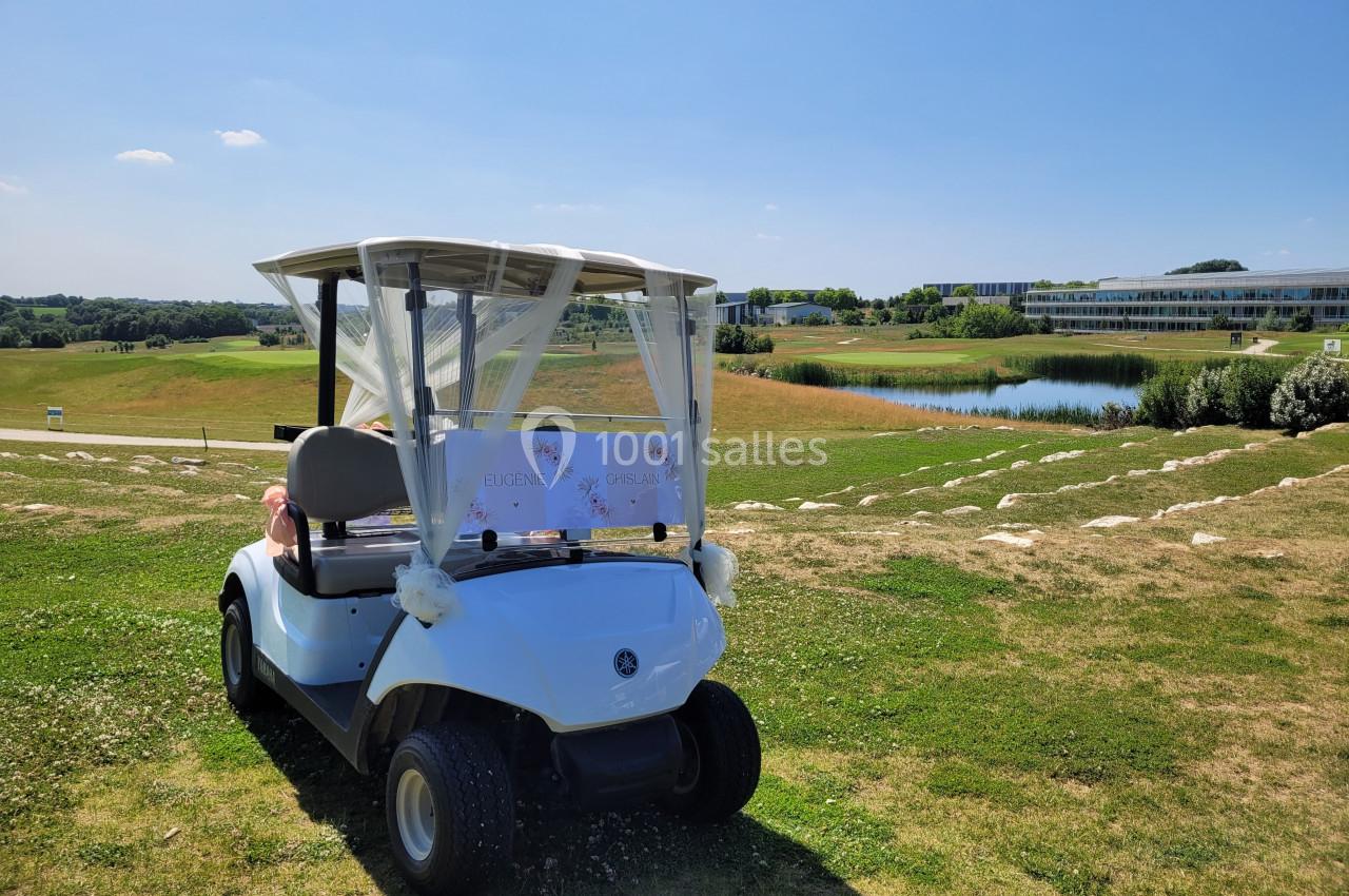 Voiturette de golf blanche décorée, stationnée sur une pelouse avec vue sur un parcours de golf et un étang.