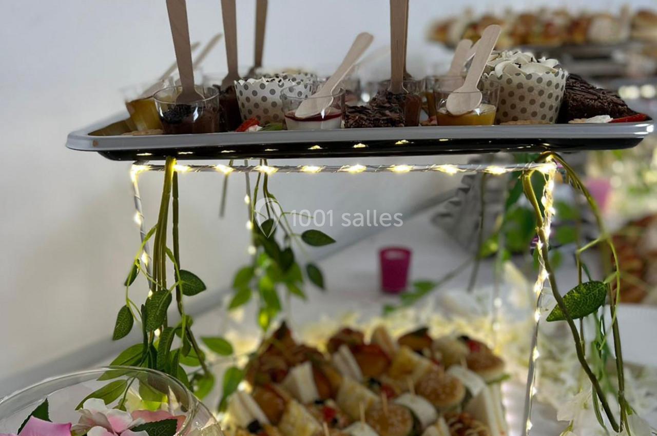 Plateau de desserts variés et mini-burgers disposés sur une table décorée de guirlandes lumineuses et de feuillage.