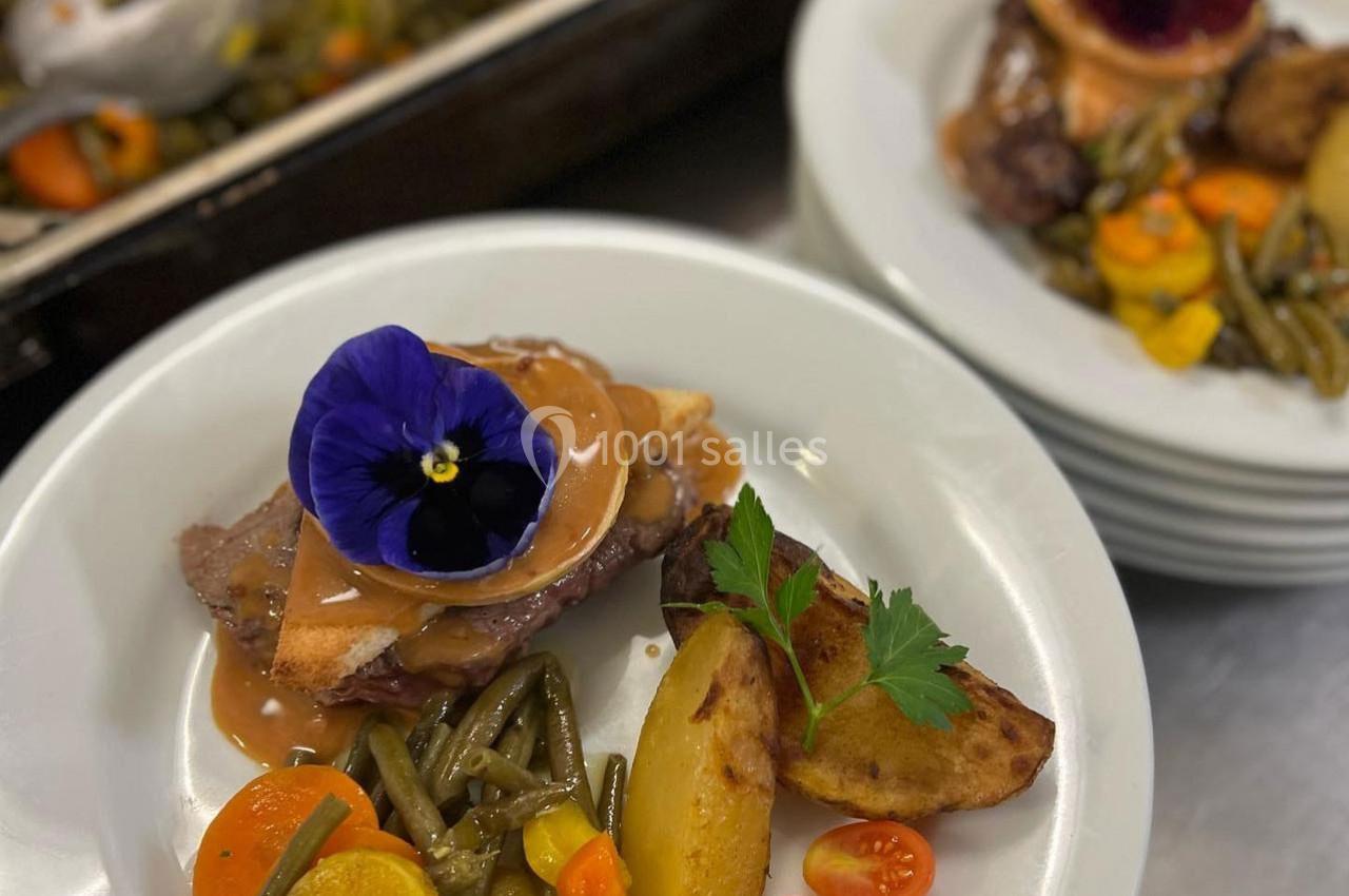 Assiette garnie de viande, légumes variés, pommes de terre rôties et fleur comestible en décoration.