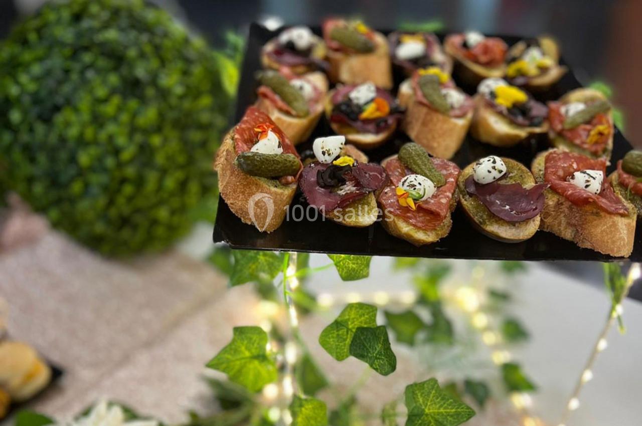 Plateau de canapés variés garnis de charcuterie, cornichons et fromage, présenté sur une table décorée de verdure.