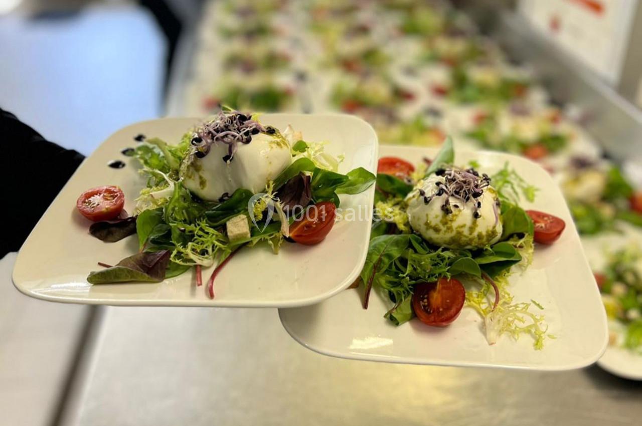 Assiettes de burrata servies sur un lit de salade verte avec tomates cerises et garniture d'herbes fraîches.