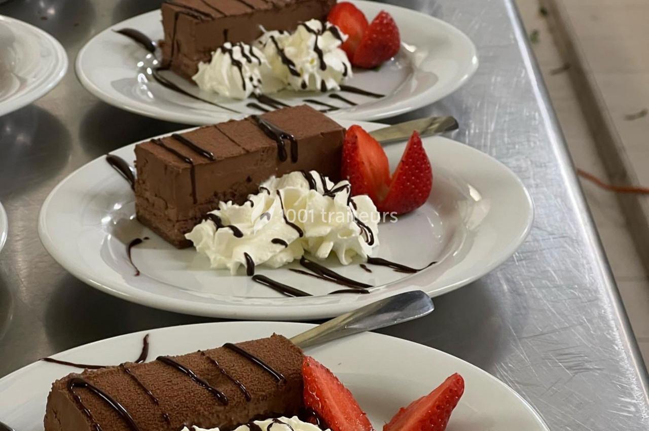 Assiettes de dessert avec parts de gâteau au chocolat, chantilly, fraises fraîches et filet de sauce chocolat.