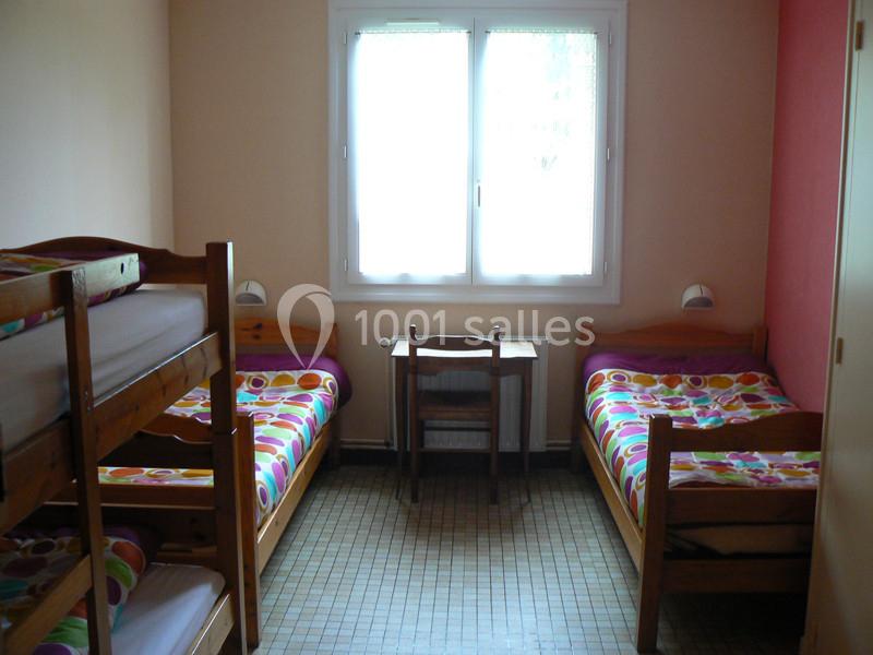 Chambre simple avec lits superposés, deux lits simples, une fenêtre et un bureau en bois clair.