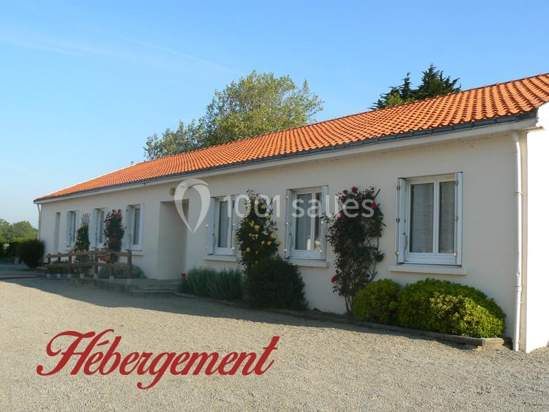 Bâtiment de plain-pied avec façade blanche, toit en tuiles rouges, et jardin fleuri devant.