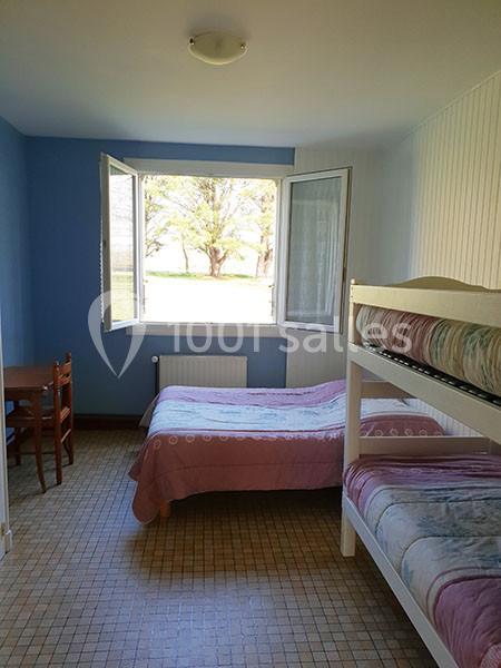 Chambre simple avec un lit double, des lits superposés, une fenêtre ouverte et un bureau en bois.