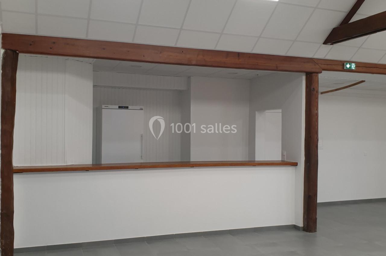 Espace intérieur avec comptoir en bois, murs blancs, plafond à dalles et sol en carrelage gris.