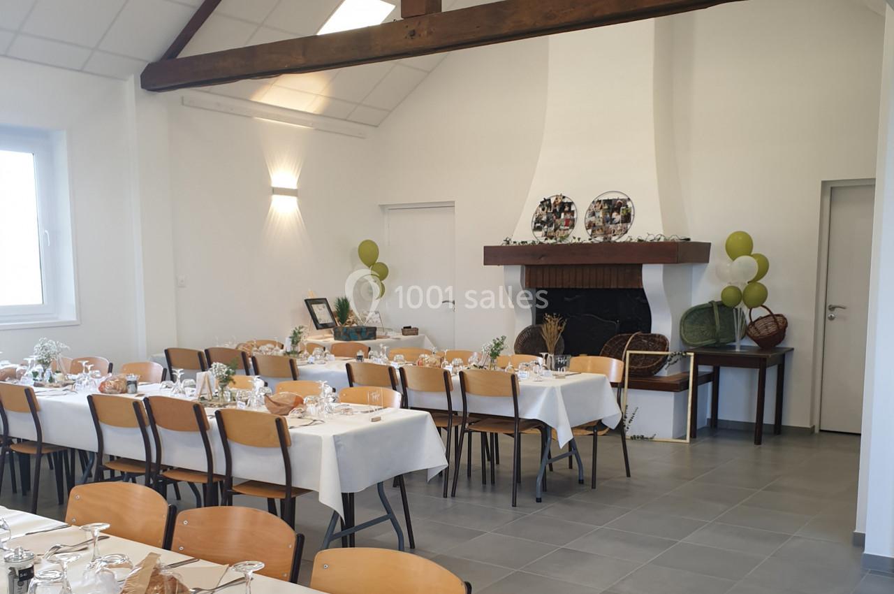 Salle décorée pour un événement avec tables dressées, chaises en bois, cheminée ornée et ballons verts en arrière-plan.