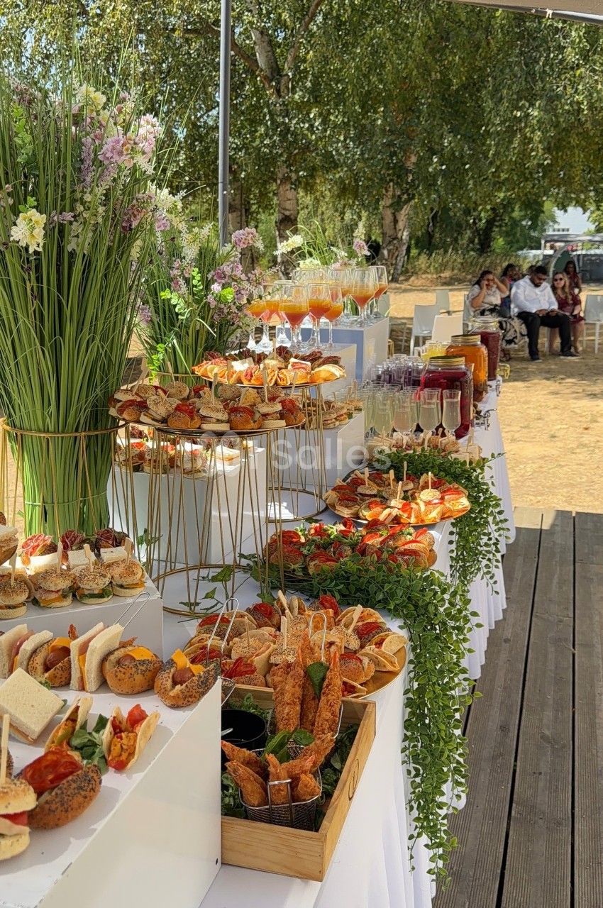 Buffet en plein air avec une variété de plats, boissons et décorations florales, installé sous une tente.