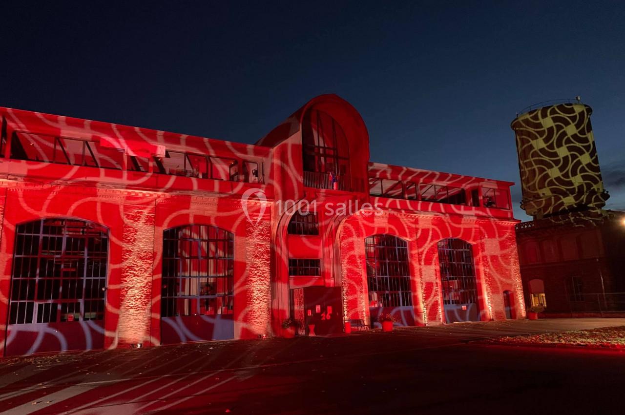 Façade d'un bâtiment illuminée par des projections rouges et blanches, avec une tour décorée à droite.