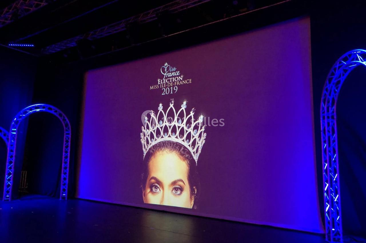 Écran de scène affichant une couronne et le visage partiel d'une femme avec le texte ’Miss Île-de-France 2019’.
