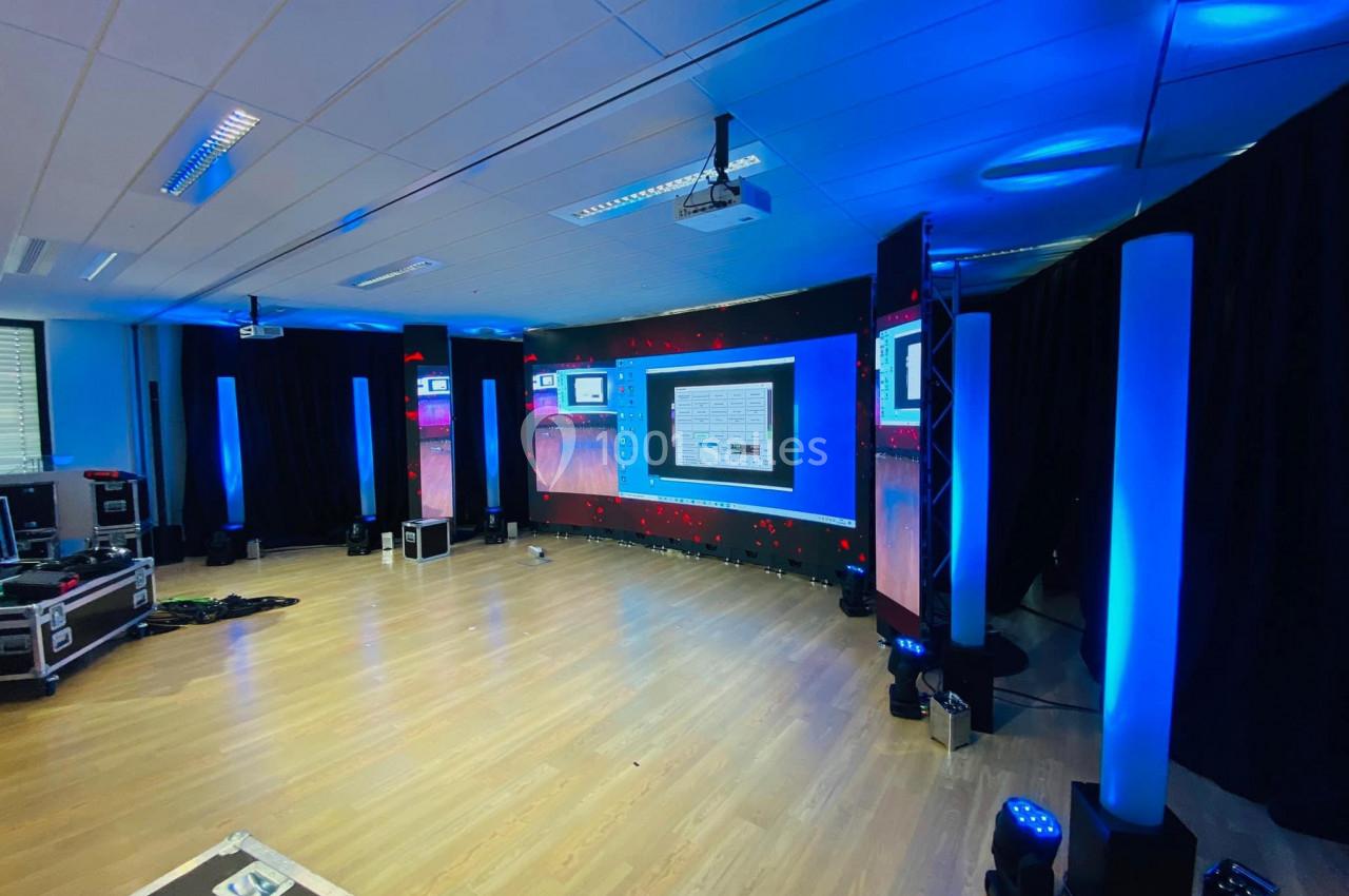 Salle équipée de plusieurs écrans, éclairages bleus et matériel audiovisuel, prête pour un événement ou une présentation.