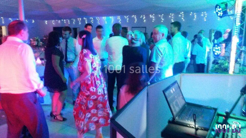 Personnes dansant et discutant dans une salle éclairée par des lumières colorées, avec un poste de DJ au premier plan.