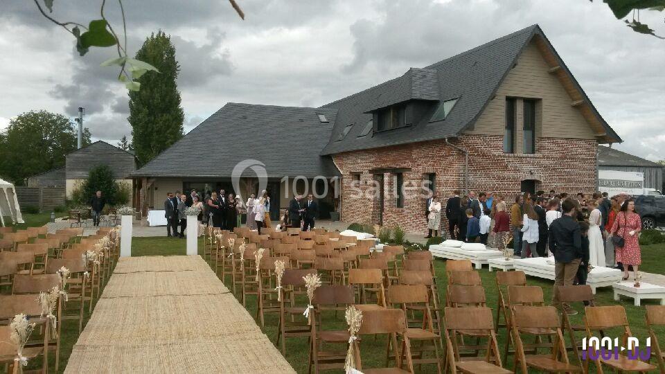 Chaises alignées et allée centrale en extérieur devant une grande maison en briques, avec des invités rassemblés au fond.