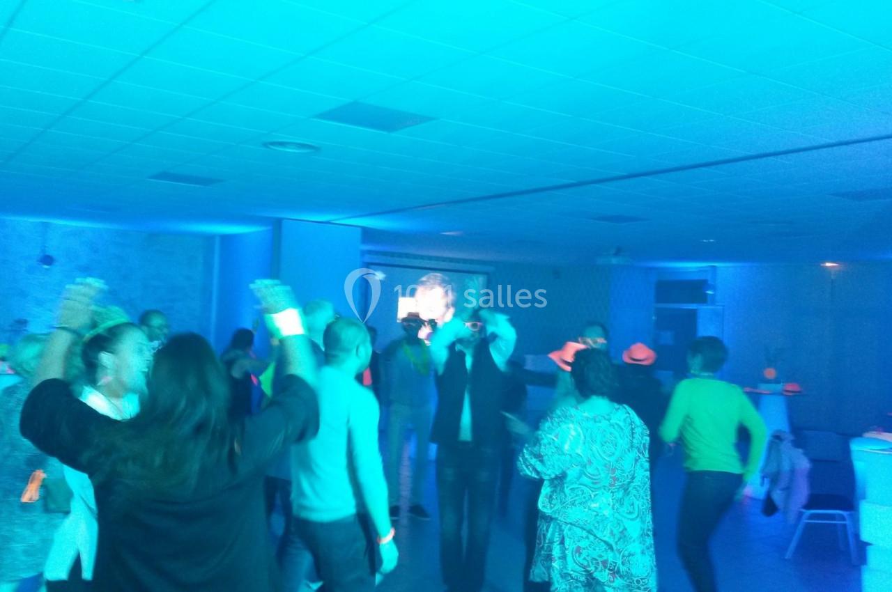 Des personnes dansent dans une salle éclairée par une lumière bleue, avec des accessoires lumineux.