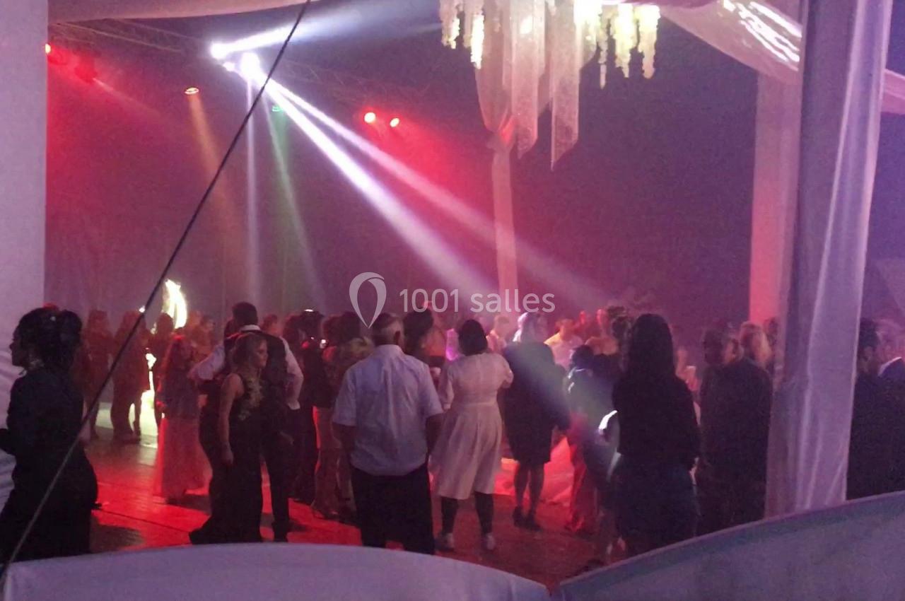 Des personnes dansent sous des lumières colorées dans une salle décorée avec des tentures et un lustre suspendu.