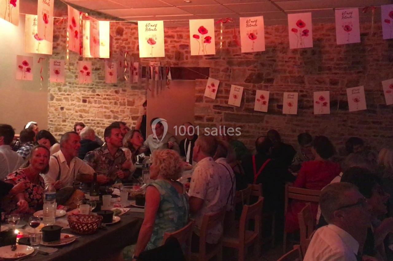 Des personnes assises à des tables dans une salle décorée de guirlandes et affiches avec des coquelicots.
