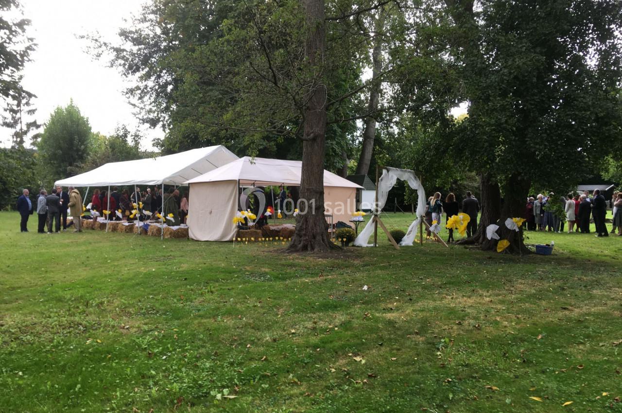 Tentes blanches installées dans un parc verdoyant, entourées de personnes et de décorations florales jaunes.
