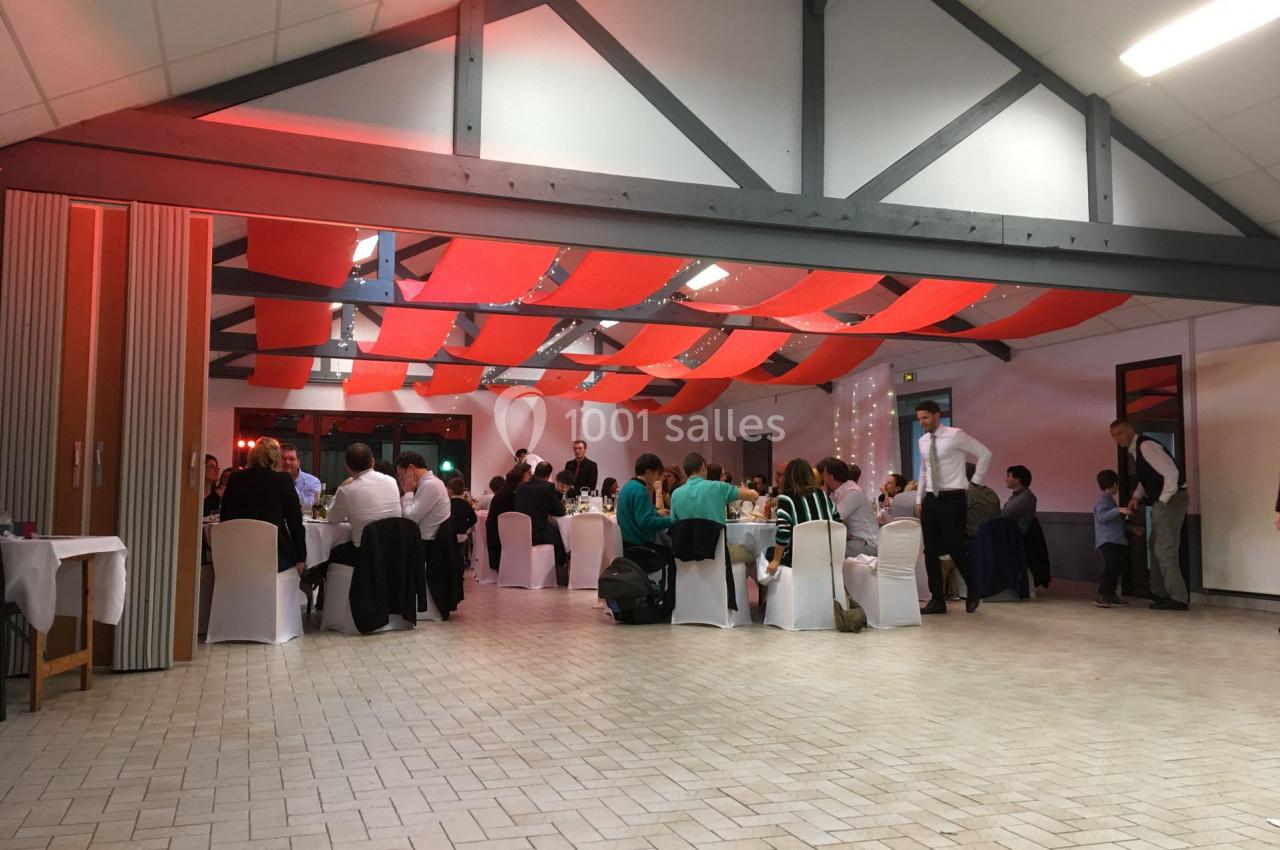 Salle de réception avec des invités assis à des tables rondes, sous un plafond décoré de bandes rouges.