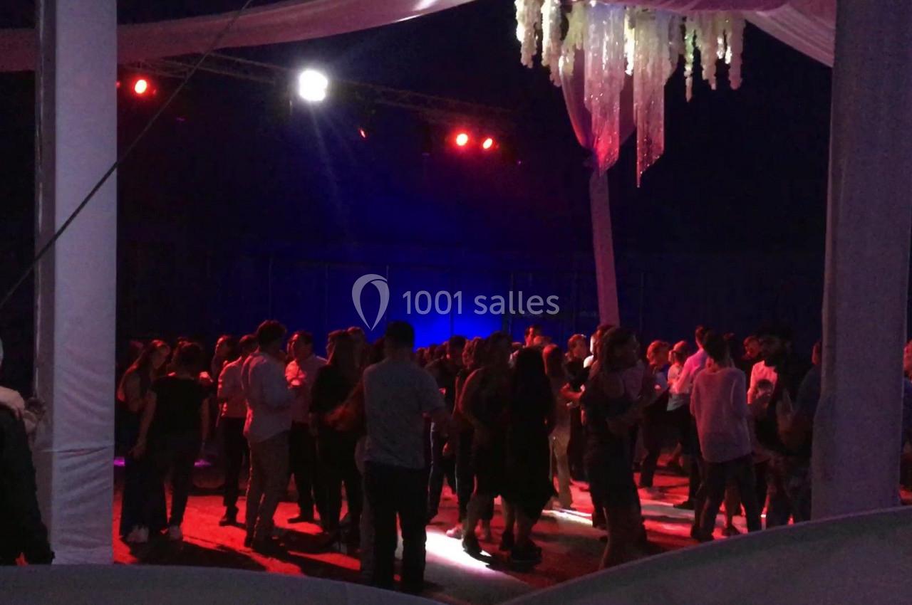 Groupe de personnes dansant sous un éclairage rouge dans une salle décorée avec des drapés et des suspensions lumineuses.