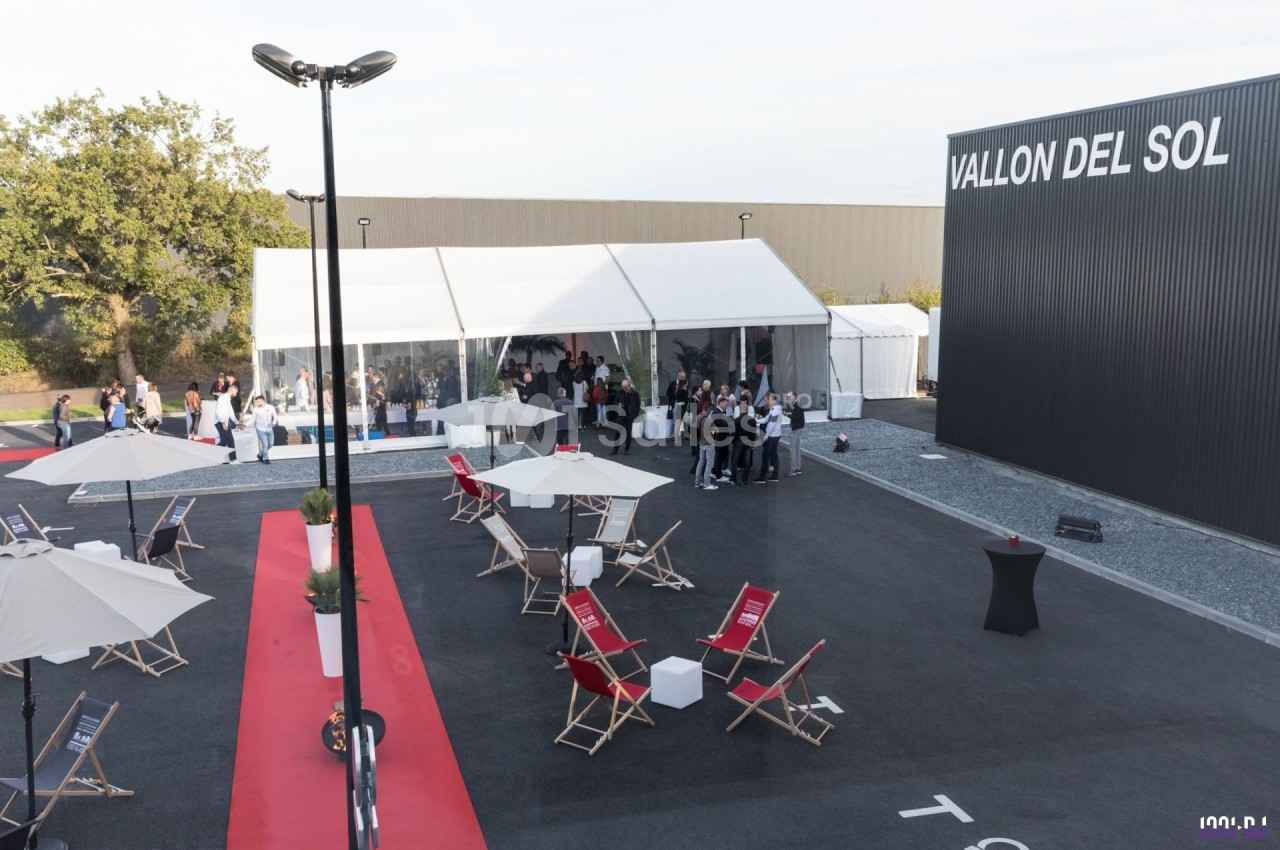 Vue d'un événement en extérieur avec des chaises longues, parasols, tapis rouge et une tente blanche accueillant des…