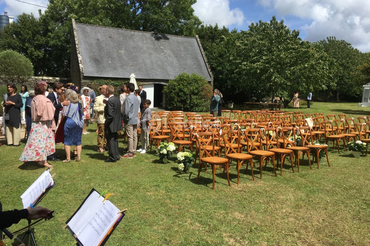 Chaises en bois disposées en rangées sur une pelouse pour une cérémonie en plein air, avec des invités rassemblés à l…