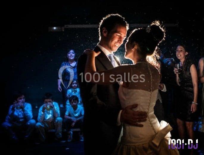 Un couple danse sous une lumière tamisée, entouré d'invités observant la scène dans une ambiance festive.