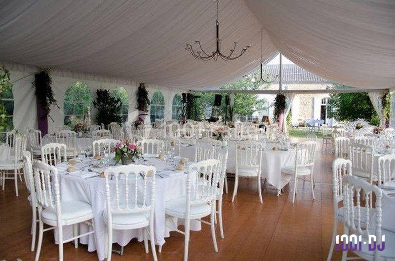 Salle de réception sous une tente blanche, tables rondes dressées avec nappes blanches et chaises élégantes.