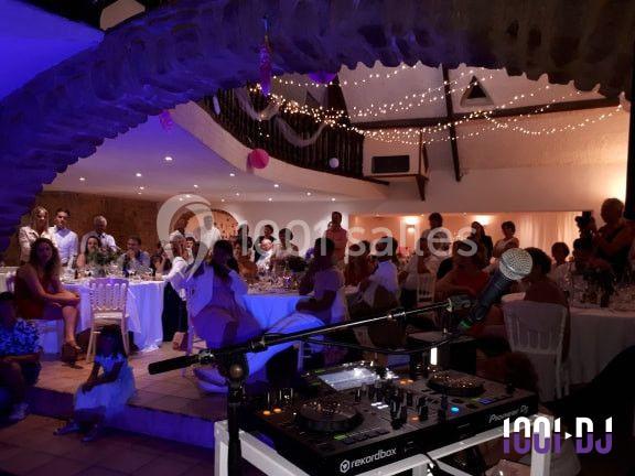 Salle de réception décorée avec des guirlandes lumineuses, des invités assis et une table de mixage au premier plan.