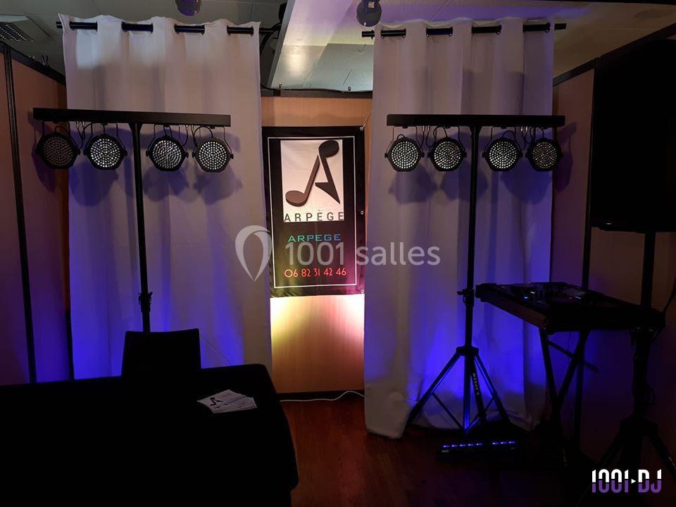 Installation d'éclairage avec spots LED colorés, rideaux blancs en arrière-plan et table de mixage sur la droite.