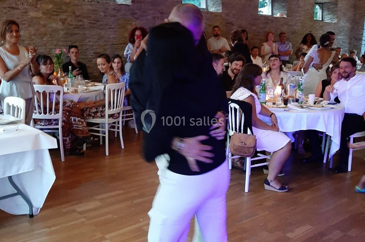 Un couple danse sur une piste en bois, portant des palmes vertes, devant des invités assis dans une salle décorée.