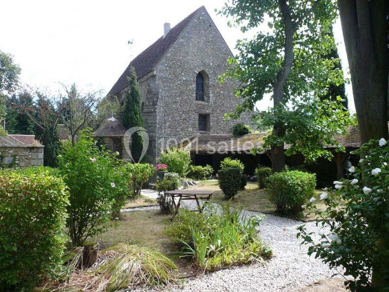 Jardin arboré avec allées gravillonnées entourant un bâtiment en pierre à toit incliné.