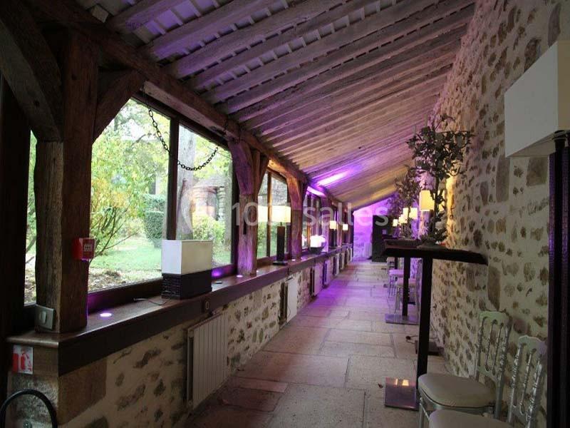 Allée couverte en pierre avec éclairage violet, murs en pierre apparente et vue sur un jardin extérieur.