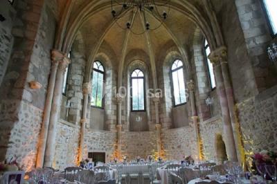 Ruelle pavée bordée de fleurs, avec un puits en pierre et des bâtiments anciens sous un ciel ensoleillé.