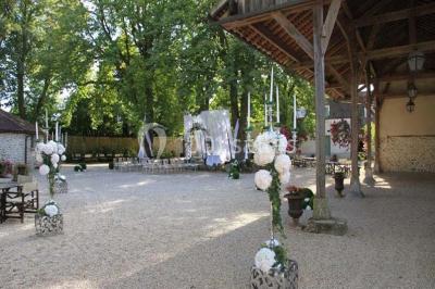 Ruelle pavée bordée de fleurs, avec un puits en pierre et des bâtiments anciens sous un ciel ensoleillé.