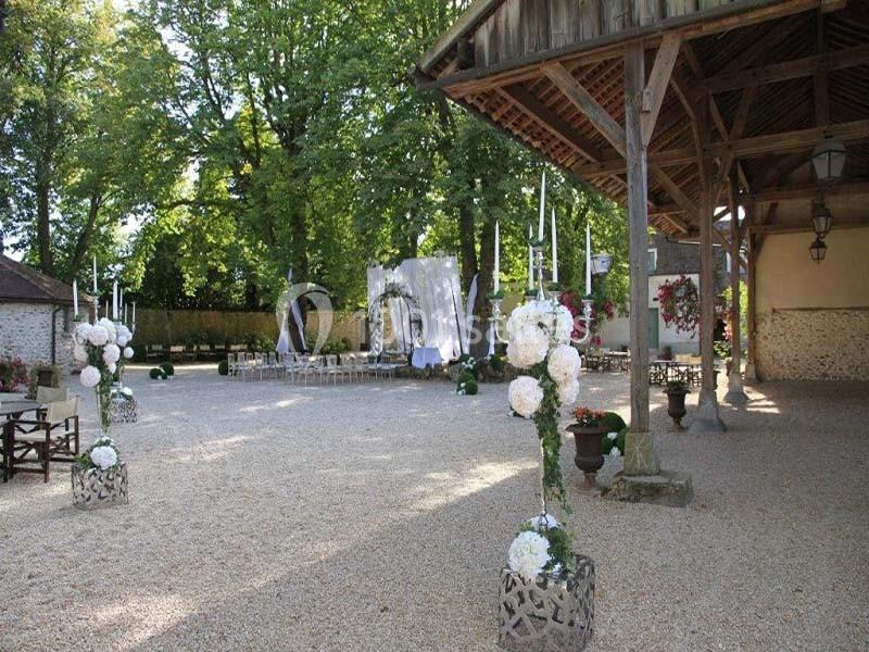 Cour extérieure aménagée pour un événement, avec des décorations florales, des chaises et un espace couvert en bois.