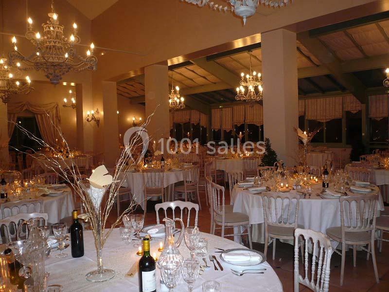 Salle de réception élégamment décorée avec des tables rondes dressées, chandeliers et ambiance lumineuse chaleureuse.