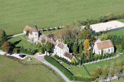 Ruelle pavée bordée de fleurs, avec un puits en pierre et des bâtiments anciens sous un ciel ensoleillé.