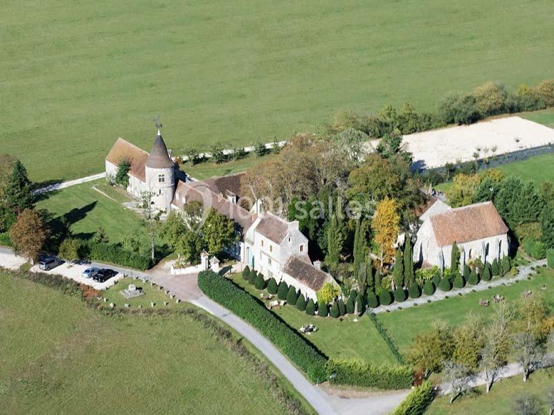 Vue aérienne d'un domaine rural avec bâtiments anciens, une tour, des jardins et des champs environnants.