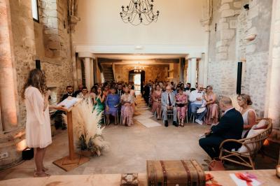 Ruelle pavée bordée de fleurs, avec un puits en pierre et des bâtiments anciens sous un ciel ensoleillé.