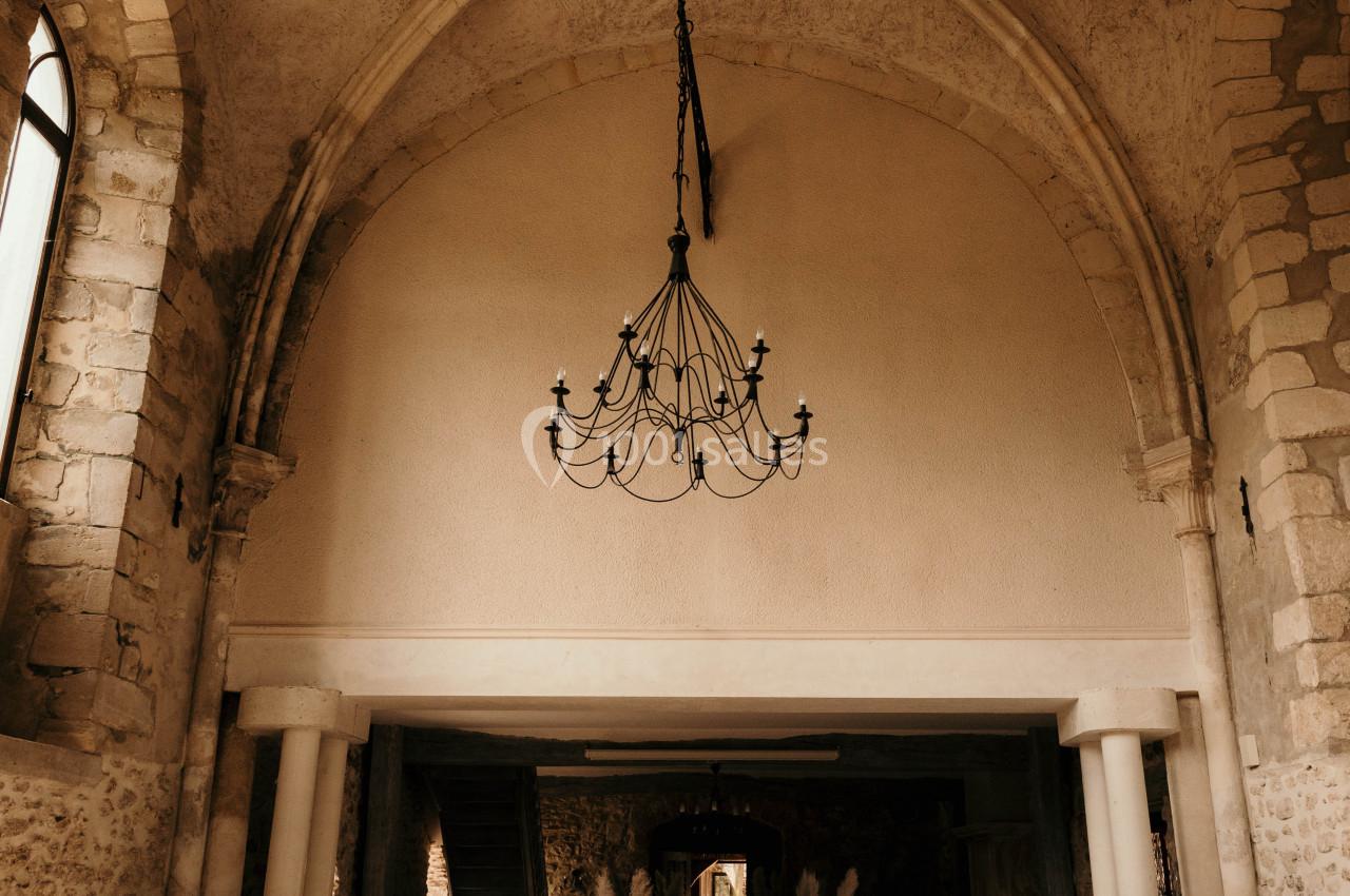 Intérieur d'une ancienne église avec des voûtes en pierre, des chaises blanches alignées et un lustre suspendu.