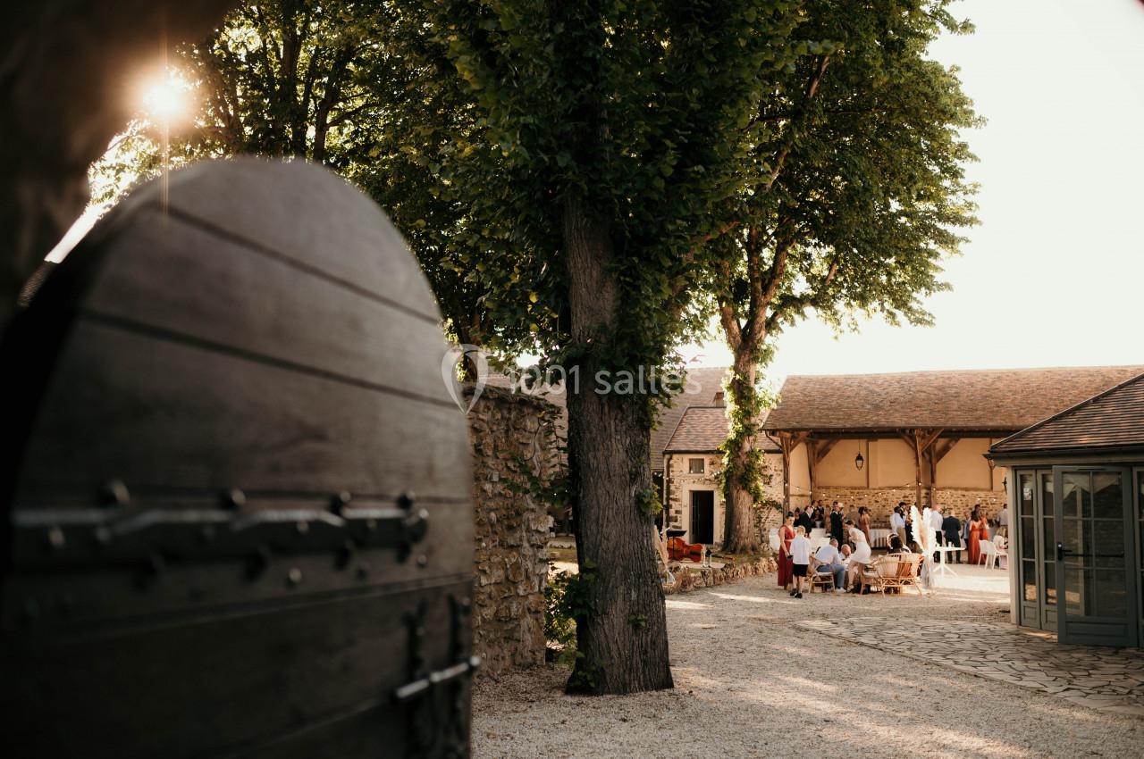 Cour intérieure d'un bâtiment en pierre, avec des invités rassemblés sous des arbres par une journée ensoleillée.