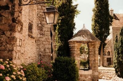 Ruelle pavée bordée de fleurs, avec un puits en pierre et des bâtiments anciens sous un ciel ensoleillé.
