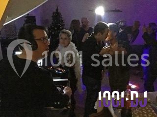 Un DJ anime une soirée dansante avec des invités qui discutent et dansent dans une ambiance tamisée.