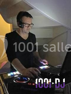 Un DJ mixe de la musique sur une console éclairée dans un environnement intérieur faiblement éclairé.