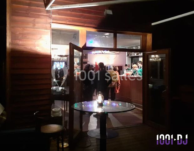 Vue nocturne d'une entrée de bar avec des portes ouvertes, des clients discutant à l'intérieur et une table éclairée au…