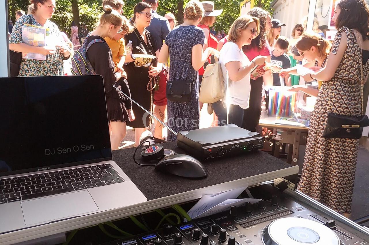 Table de mixage et ordinateur sous une tente, avec des personnes rassemblées autour de stands en arrière-plan.