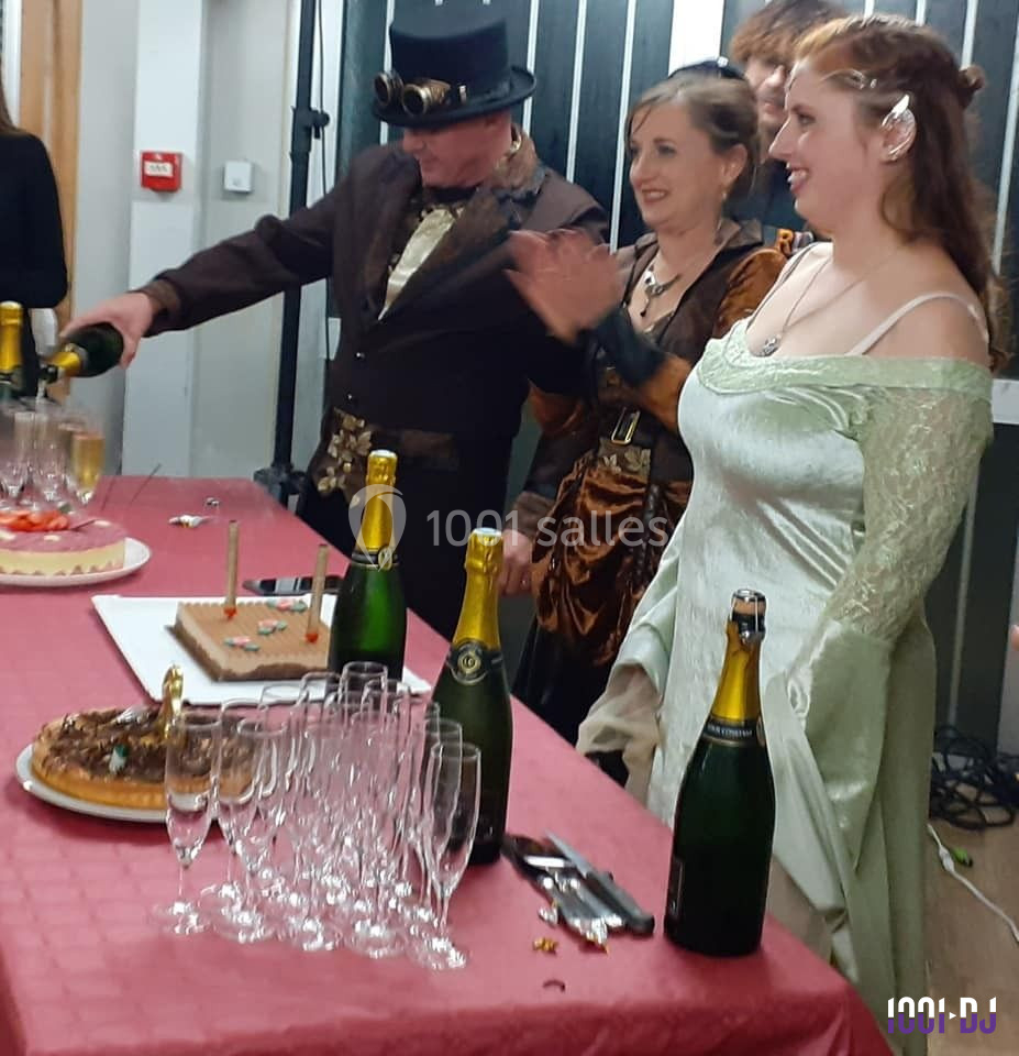 Des personnes en tenue rétro-futuriste célèbrent autour d'une table avec gâteaux, verres et bouteilles de champagne.
