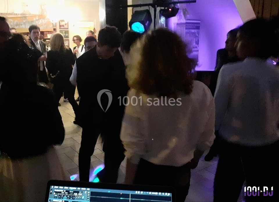 Des personnes dansent dans une ambiance festive avec des lumières colorées, vue partielle d'une table de mixage au premier…