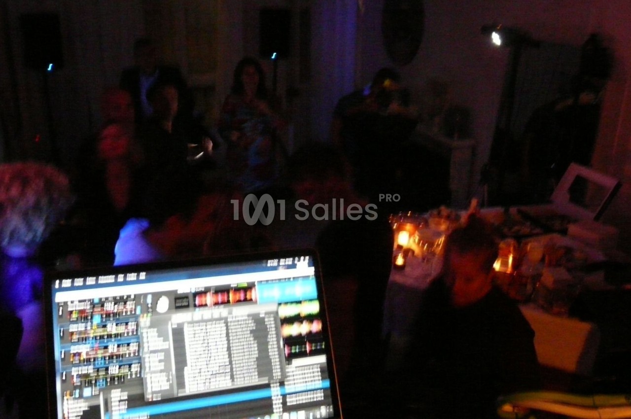 Vue d'une soirée avec un DJ en arrière-plan, des invités dans une ambiance tamisée et un écran de mixage au premier plan.